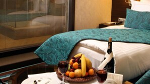 Habitació d'hotel amb llit, taula de dinar amb plats, coberts i una cistella de fruita.