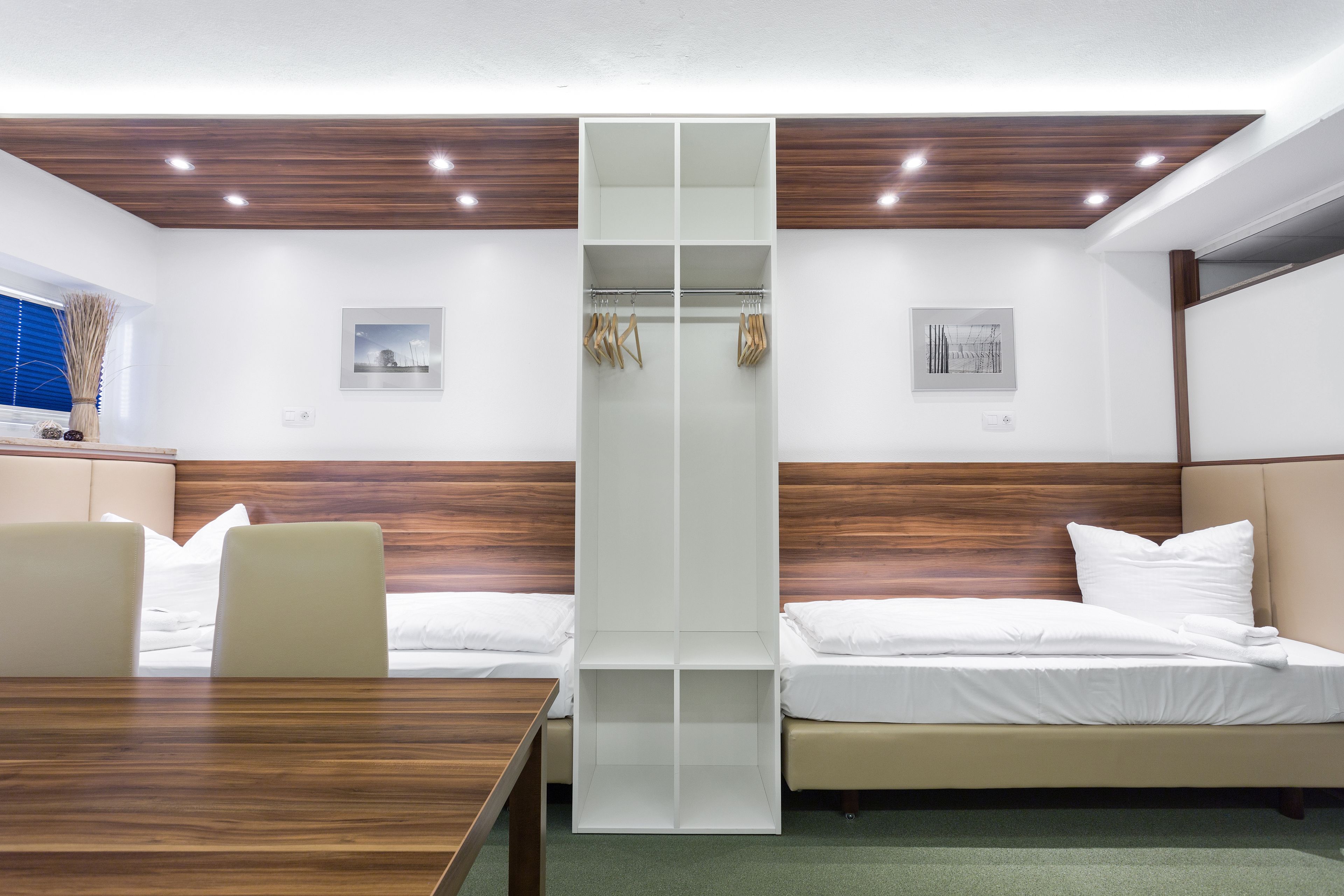 A hotel room with a wooden ceiling, two beds, a table, and a wardrobe.