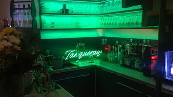 A bar area with shelves of bottles and glasses, a neon sign reading "Tanqueray", and a keyboard on the counter.