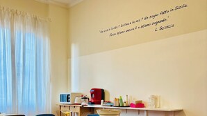 A dining area with a white table and red chairs, a kitchen area with appliances, and a quote on the wall. - Castelnuovo Rooms  (Palermo)