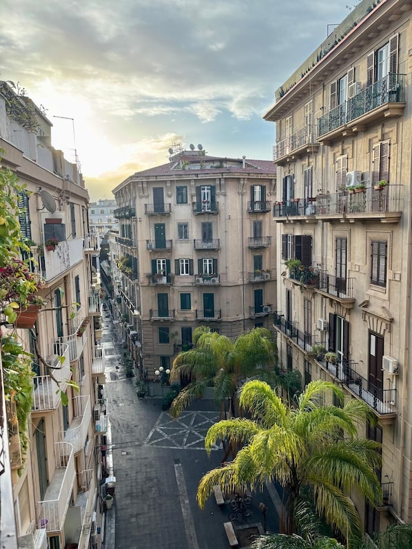 A narrow urban street flanked by multi-story buildings with balconies, some with plants.