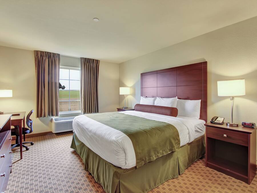 Ein Hotelzimmer mit einem großen Bett, einem Schreibtisch, einem Sessel, einem Nachttisch mit Lampe und einem Fenster mit Vorhängen.