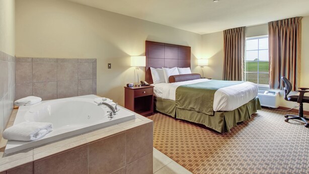 A hotel room with a large bed, a separate bathroom with a bathtub, a desk, and a window with curtains. - Cobblestone Hotel & Suites - Waynesboro (Waynesboro)