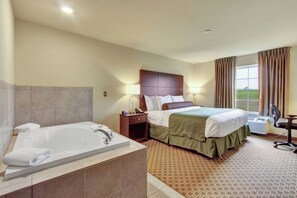 Ein Hotelzimmer mit einem großen Bett, einem separaten Badezimmer mit Badewanne, einem Schreibtisch und einem Fenster mit Vorhängen.