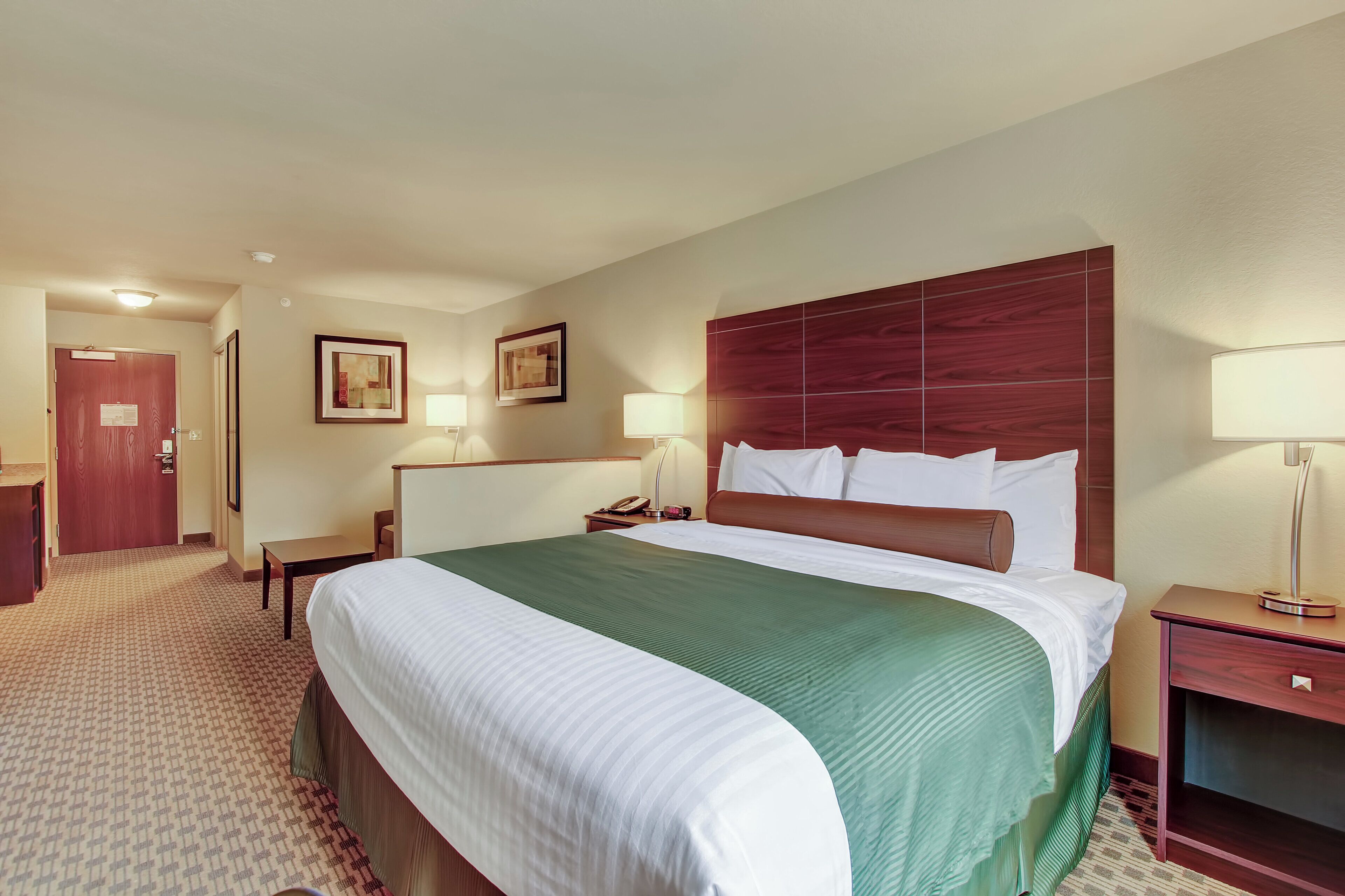 A hotel room with a large bed, a wooden headboard, two bedside tables with lamps, a desk, and a chair.