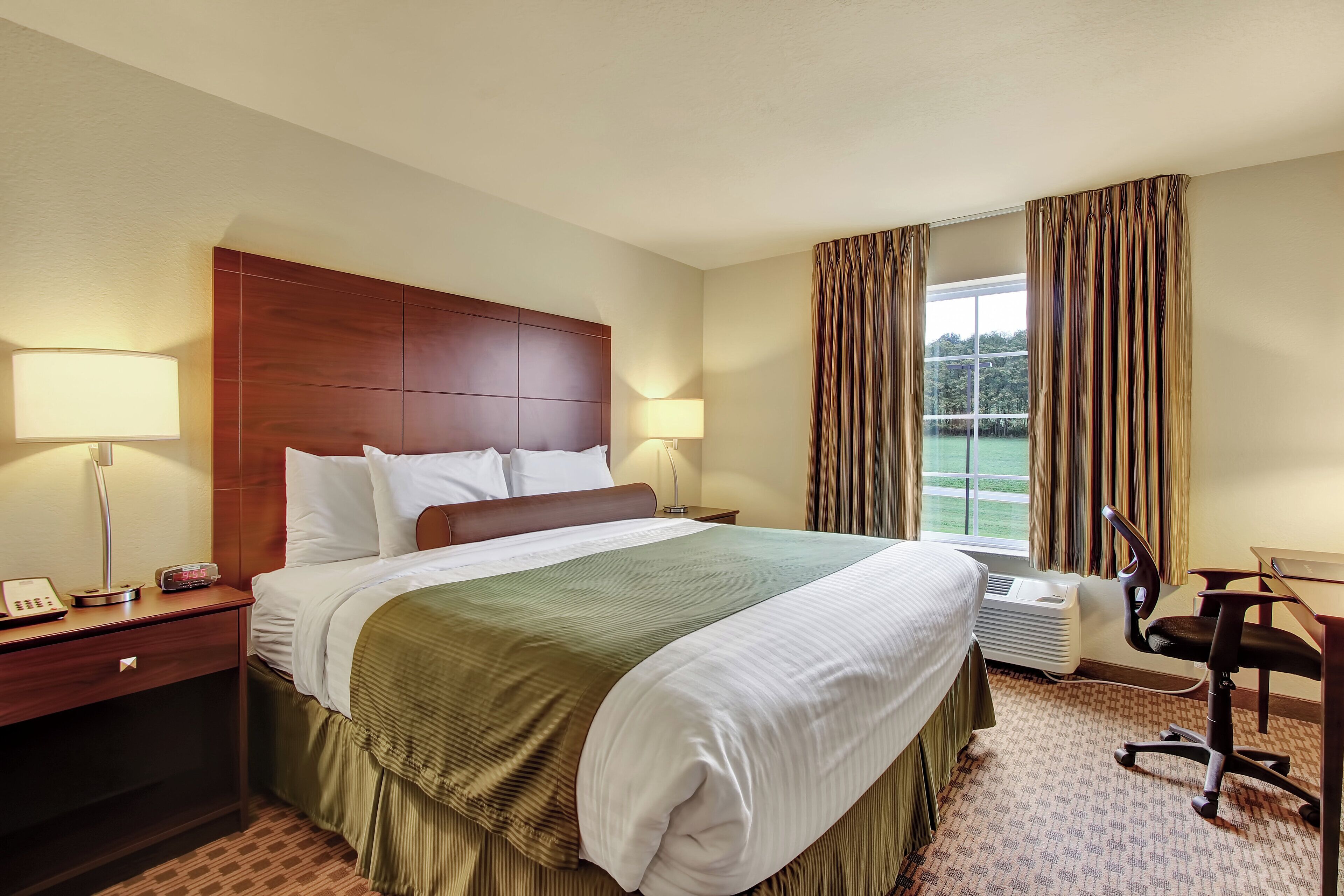 Une chambre d’hôtel avec un grand lit, deux lampes de chevet, un bureau avec une chaise et une fenêtre avec des rideaux.