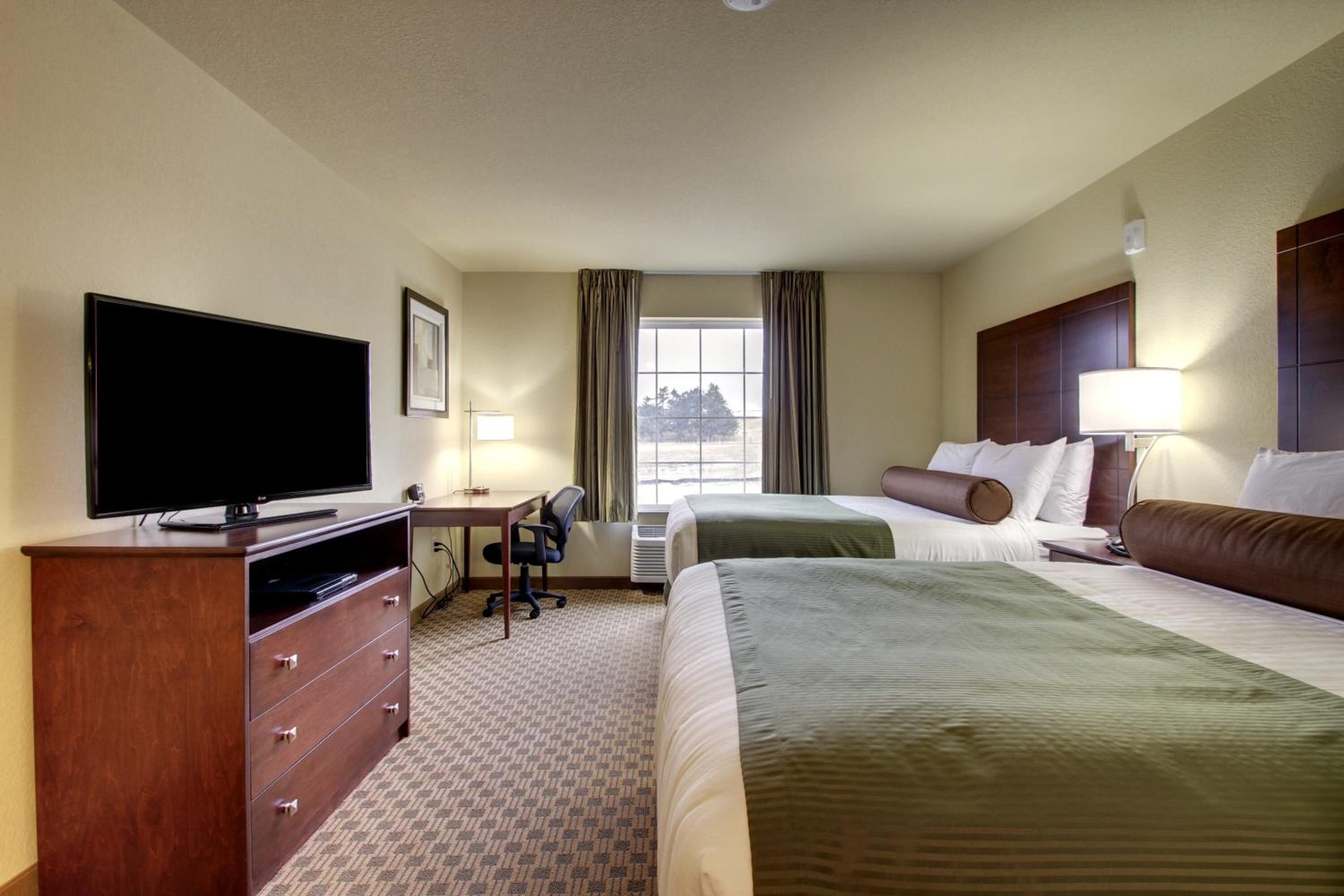 A hotel room with a flat-screen TV, a desk, two beds, and a window with curtains.
