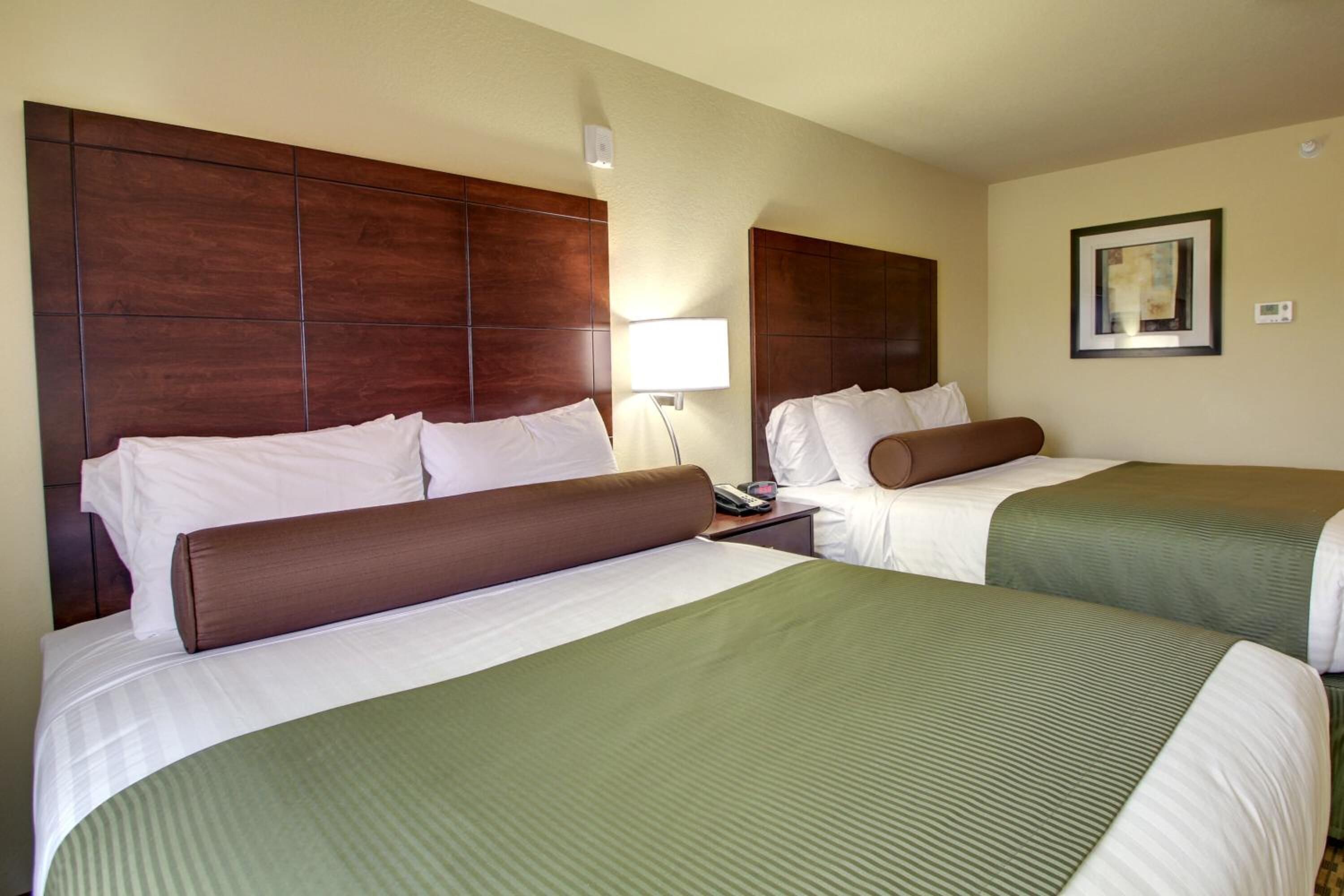 A hotel room with two beds, each with a wooden headboard, white bedding, and a green accent.