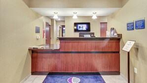 A reception area with a wooden reception desk, a flat-screen TV mounted above it, and a sign indicating check-in and check-out times. - Cobblestone Hotel & Suites - Waynesboro (Waynesboro)