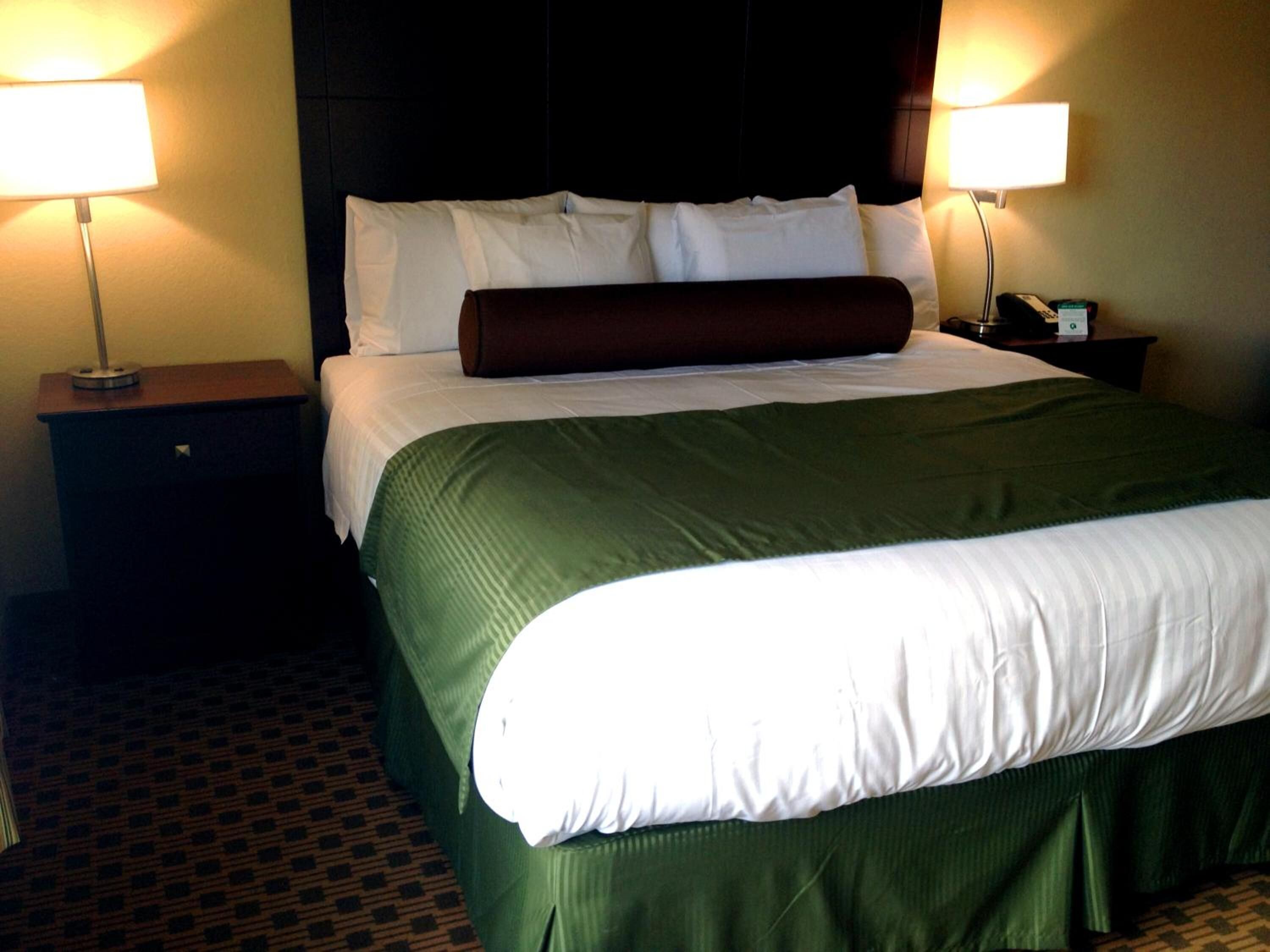 Una habitación de hotel con una cama grande, dos lámparas de noche, una mesita de noche y una alfombra estampada.