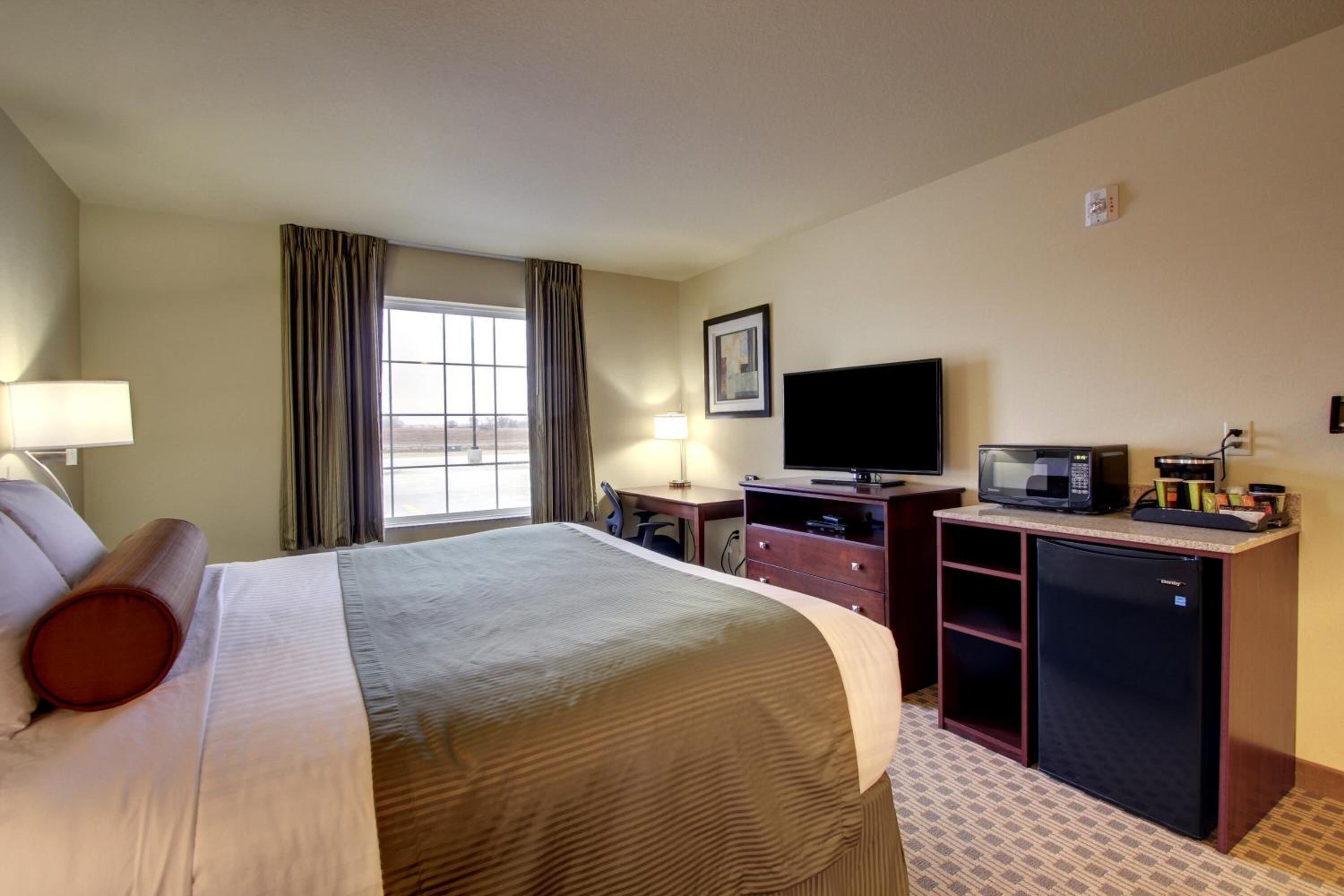 A hotel room with a large bed, a desk with a computer, a television, a microwave, and a refrigerator.