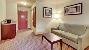 A hotel room with a sofa, a small table, a lamp, and a desk with a mirror. - Cobblestone Hotel & Suites - Waynesboro (Waynesboro)