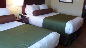 Una habitación de hotel con dos camas, cada una con ropa de cama verde y blanca, una mesita de noche con una lámpara y un cuadro en la pared.