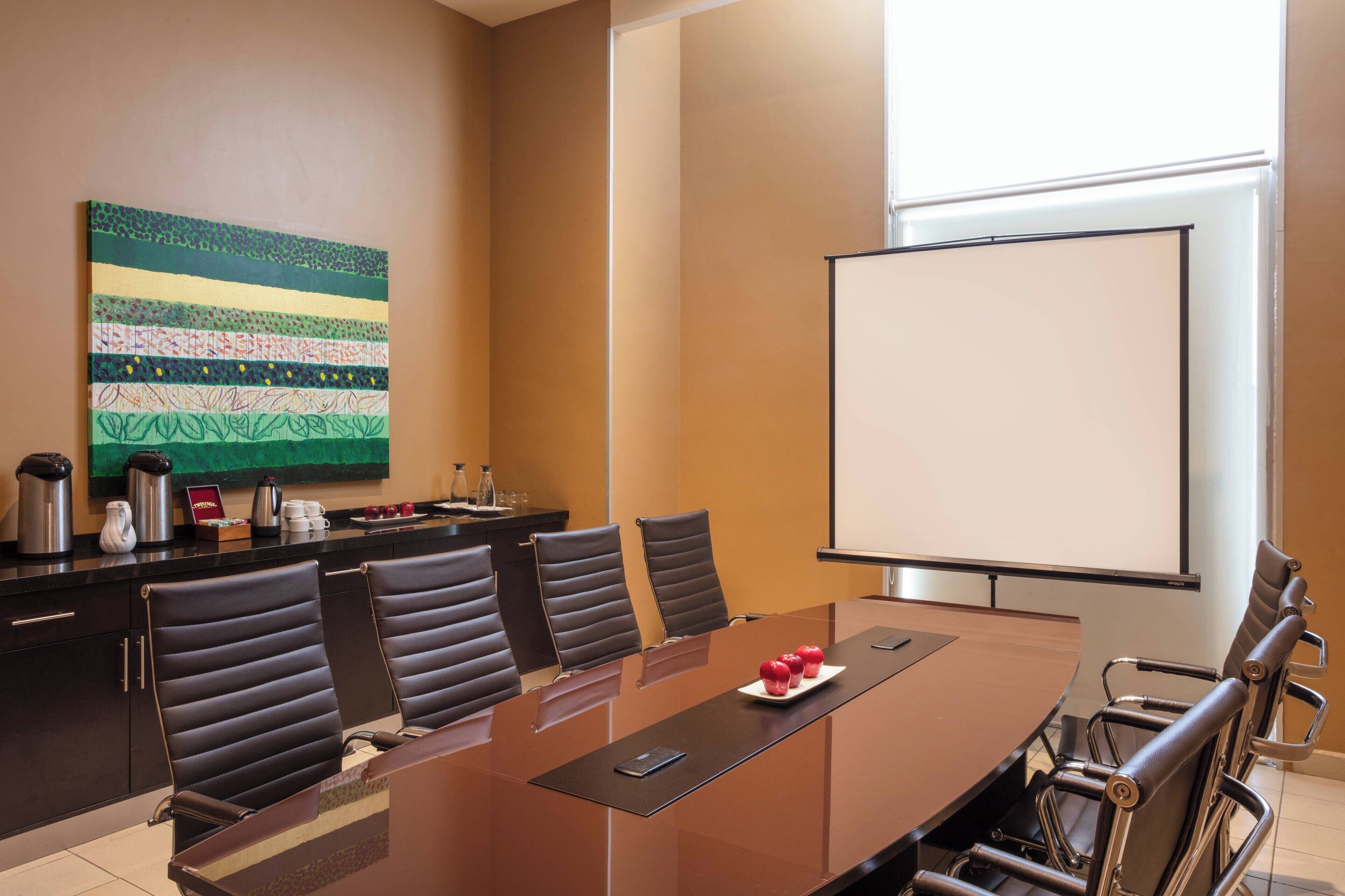 A conference room with a long table, six chairs, a projector screen, and a decorative wall piece.