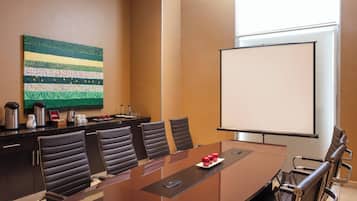 A conference room with a long table, six chairs, a projector screen, and a decorative wall piece.