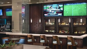 A bar area with multiple seating options, including bar stools and a long table. There are televisions mounted on the wall displaying sports events. - Courtyard by Marriott Queretaro (Querétaro)