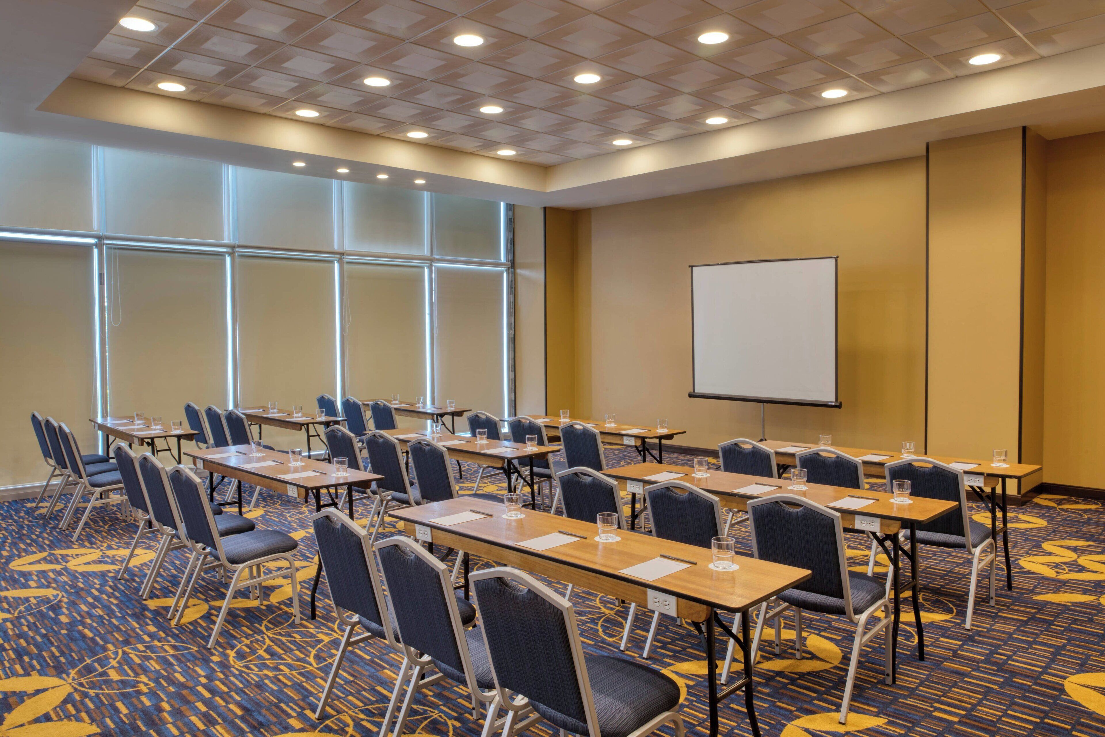 A conference room with rows of tables and chairs, a projector screen, and large windows.