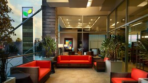 A modern lobby with a red sofa, wicker furniture, and potted plants. - Courtyard by Marriott Queretaro (Querétaro)