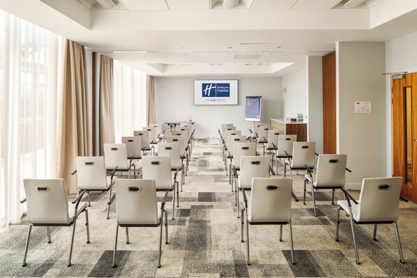 Un salón de conferencias de hotel con filas de sillas, una pantalla grande y un mostrador de recepción.