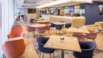 A modern hotel lobby with a bar area, seating arrangements, and a television screen.