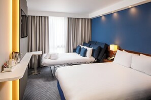 A hotel room with two beds, a desk, a chair, a lamp, and a window with curtains.