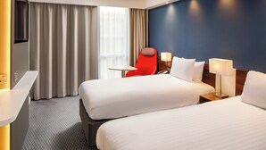 A hotel room with two beds, a red chair, a desk, and a TV. - Holiday Inn Express London - ExCeL by IHG (London)