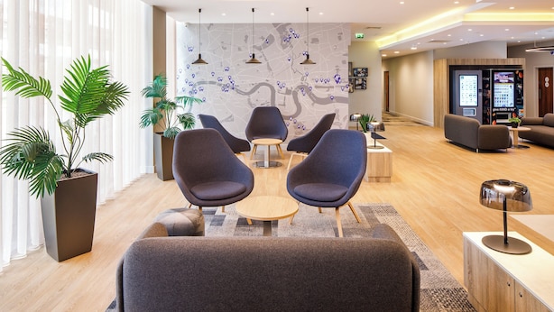 Un hall d’hôtel moderne, doté d’espaces aménagés avec des sièges, d’un comptoir de réception et d’une grande carte affichée au mur.