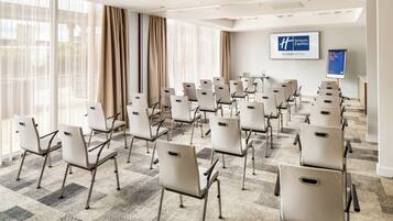Ett konferensrum med rader av stolar, stora fönster med gardiner och en skylt med texten ”Holiday Inn Express” på väggen.