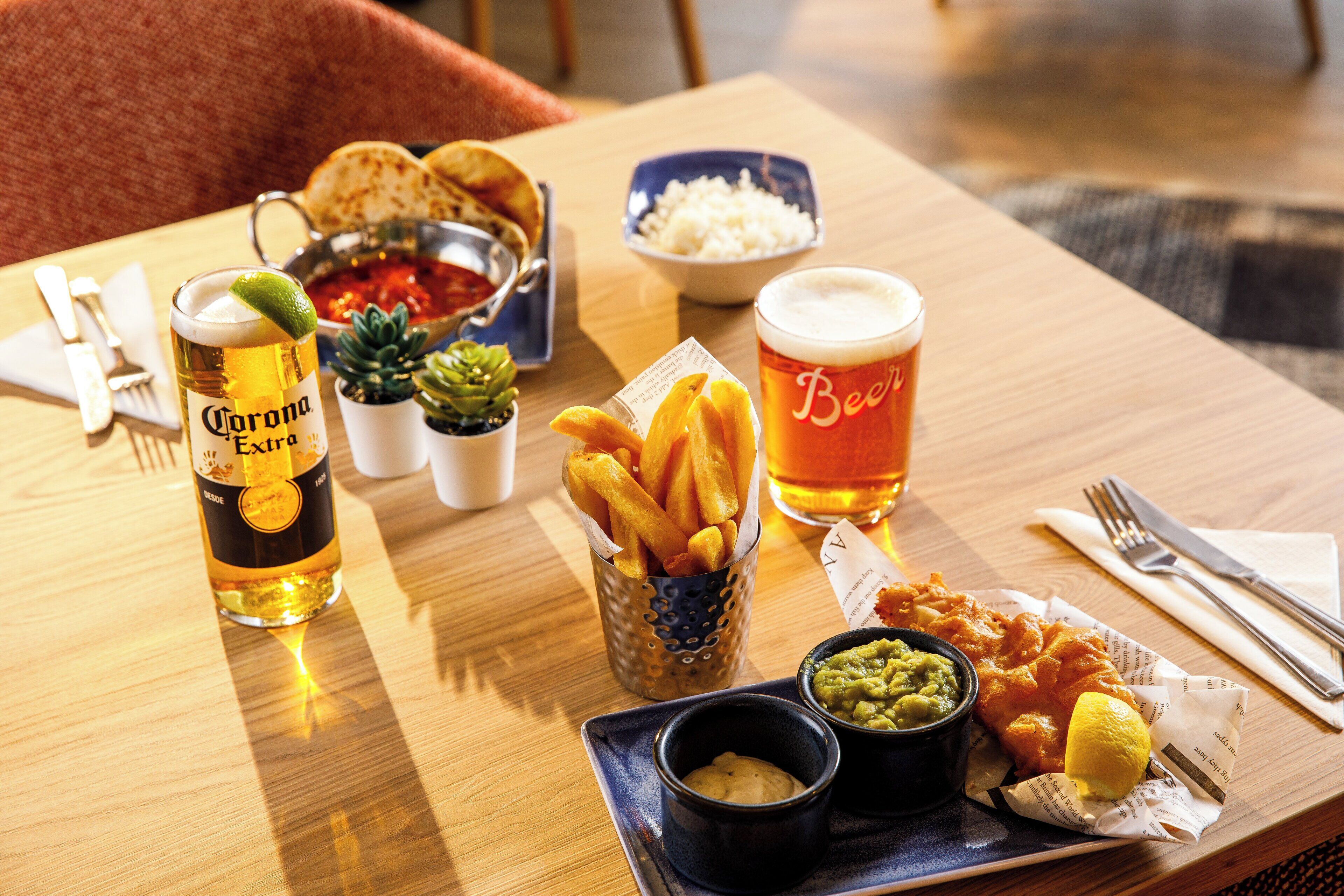A table with a beer, fries, and a small bowl of guacamole.