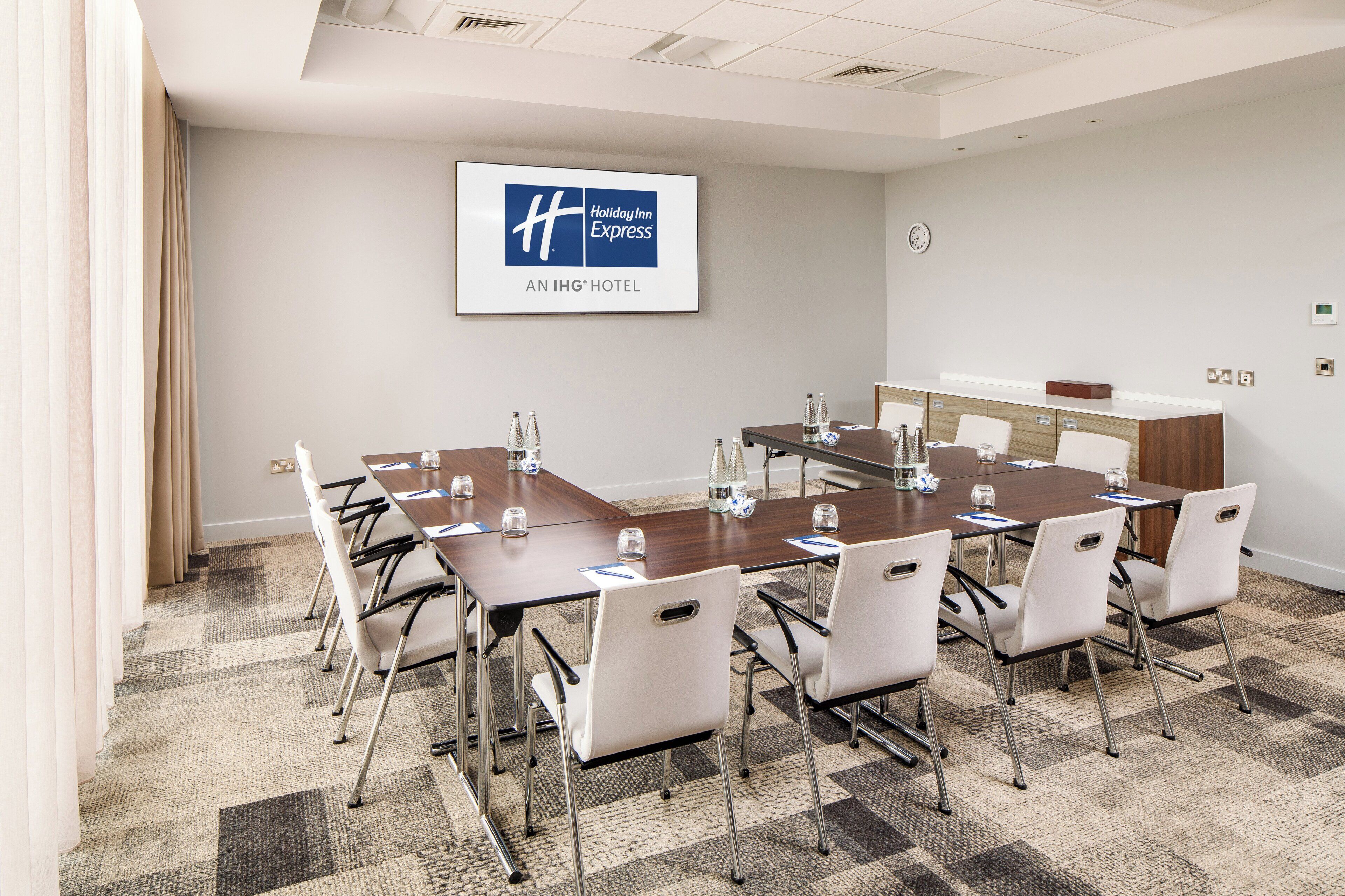 A conference room with a large table, white chairs, and a Holiday Inn Express sign on the wall.