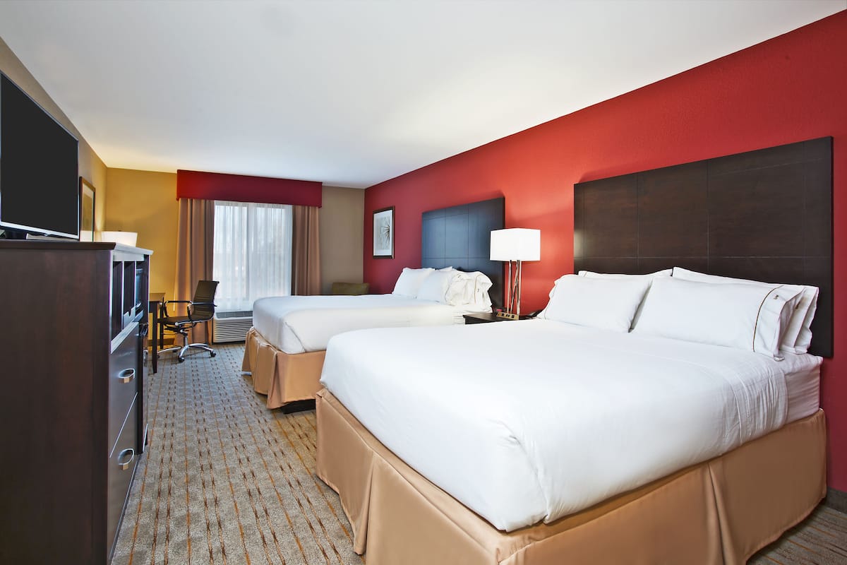 A hotel room with two beds, a desk, a chair, a TV, and a lamp.