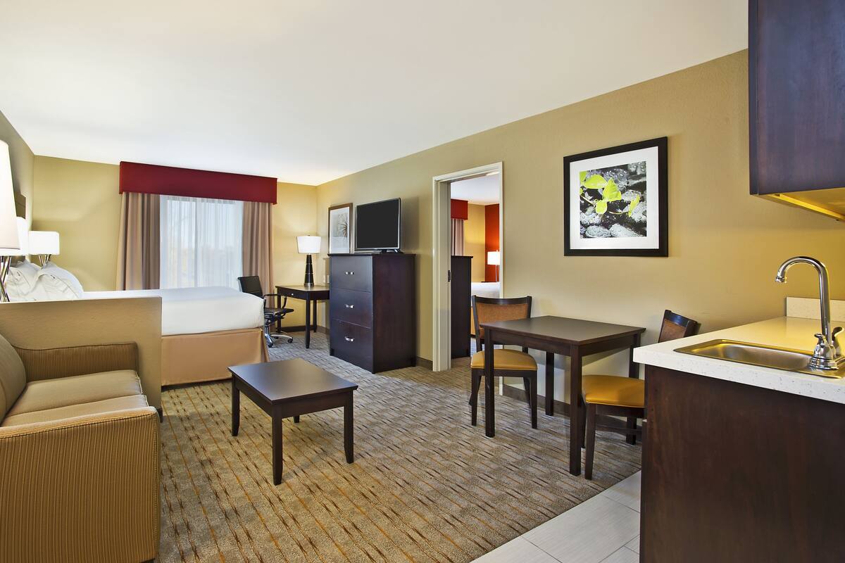 A hotel room with a bed, a desk, a chair, a small table, a TV, a cabinet, and a sink.