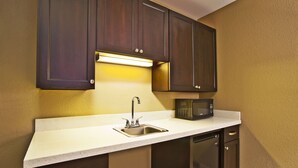 A compact kitchen with dark wood cabinets, a stainless steel sink, a microwave, and a dishwasher. - Holiday Inn Express & Suites Springfield - Dayton Area by IHG (Springfield)