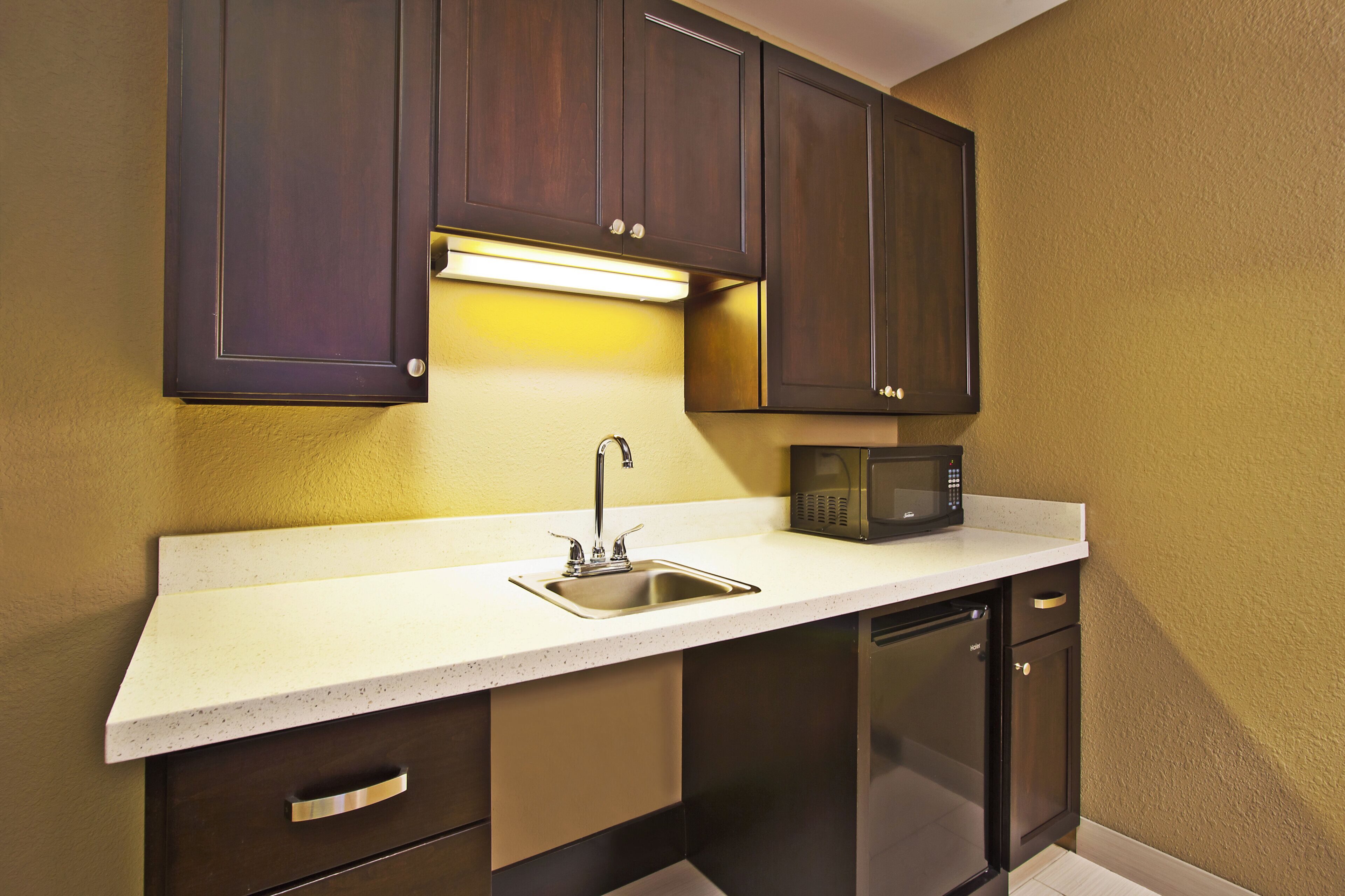 A compact kitchen with dark wooden cabinets, a stainless steel sink, and a microwave.