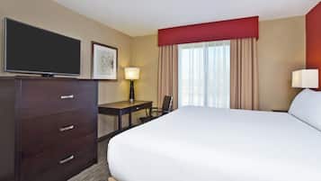 A hotel room with a large bed, a desk with a chair, a television, and a window with curtains.