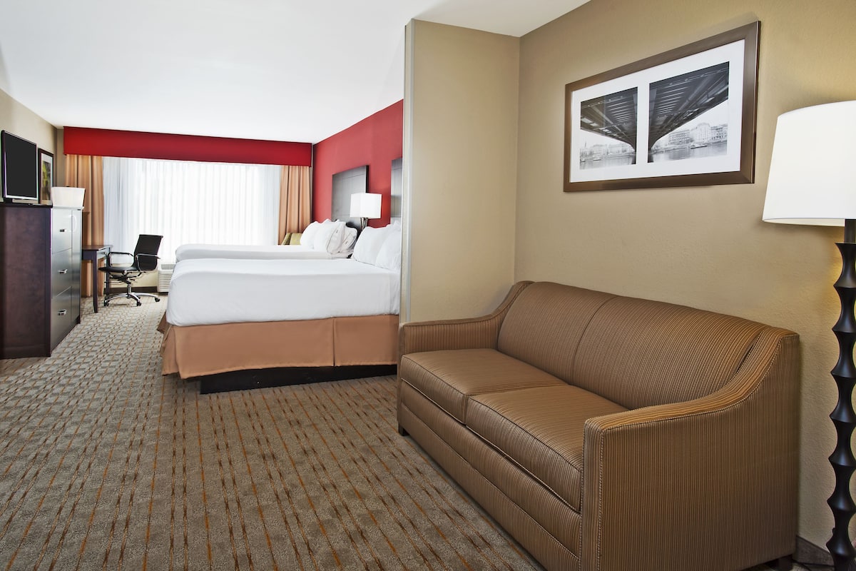 A hotel room with a large bed, a sofa, a desk with a computer, and a TV.