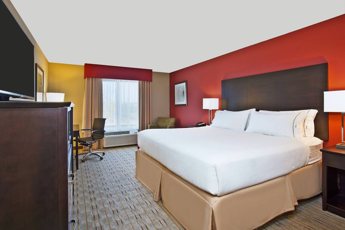 A hotel room with a large bed, a desk, a chair, and a TV.