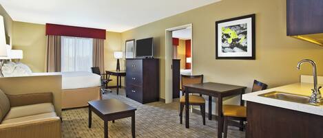 A hotel room with a bed, a desk, a chair, a dresser, a television, and a sink.