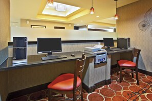 A hotel reception area with a computer desk, two bar stools, a printer, and a wall-mounted decorative piece. - Holiday Inn Express & Suites Springfield - Dayton Area by IHG (Springfield)