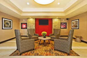 A lobby with a red accent wall, two armchairs, a round table with a potted plant, and framed artwork on the walls. - Holiday Inn Express & Suites Springfield - Dayton Area by IHG (Springfield)