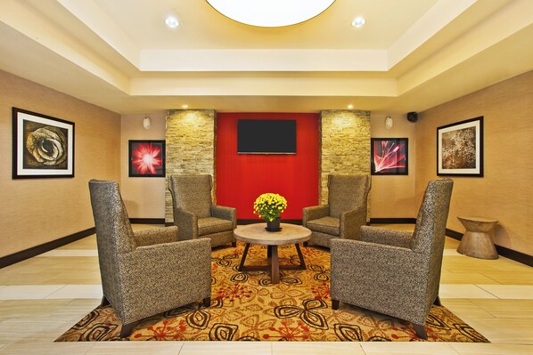 A lobby with a red accent wall, two armchairs, a round table with a potted plant, and framed artwork on the walls. - Holiday Inn Express & Suites Springfield - Dayton Area by IHG (Springfield)