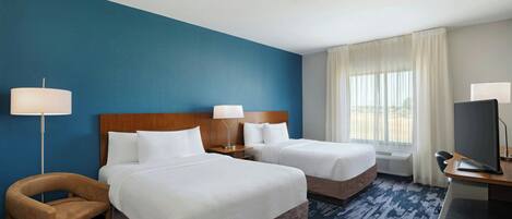 A hotel room with two beds, a desk with a TV, a chair, and a lamp.