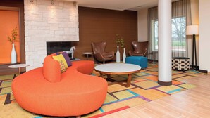A modern hotel lobby with a stone fireplace, leather armchairs, a round coffee table, and a colorful carpet. - Fairfield Inn & Suites Fredericksburg (Fredericksburg)
