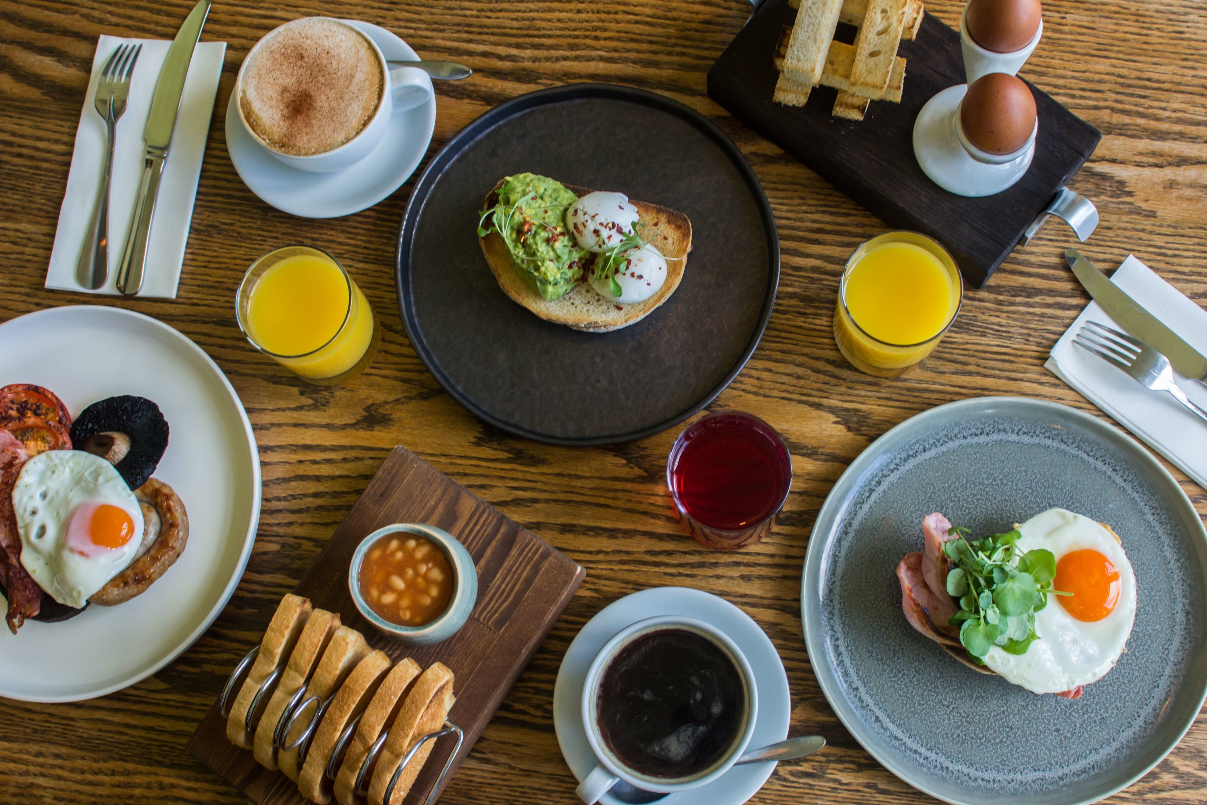 Desayuno con tostadas, huevos, frijoles y bebidas sobre una mesa de madera.