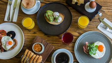 Desayuno con tostadas, huevos, frijoles y bebidas sobre una mesa de madera.