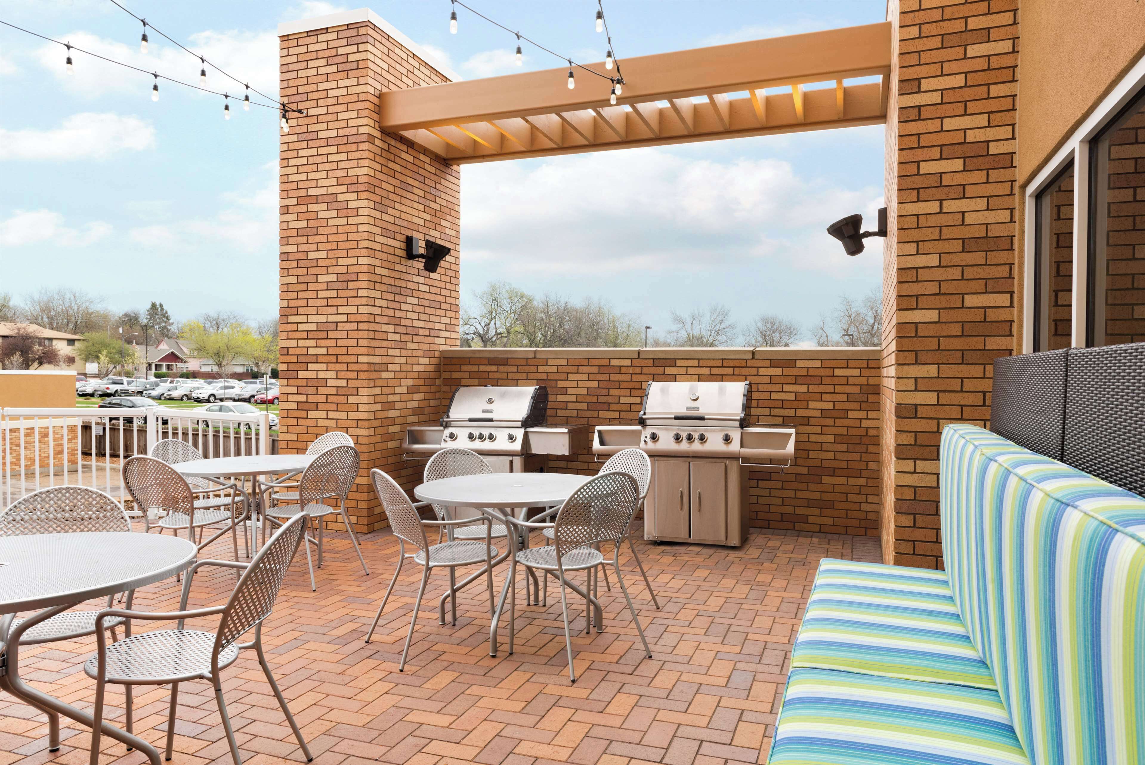 An outdoor patio with a brick wall, two grills, a table with chairs, and a striped sofa.