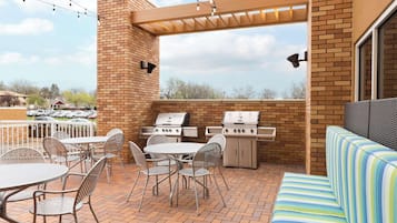 An outdoor patio with a brick wall, two grills, a table with chairs, and a striped sofa.