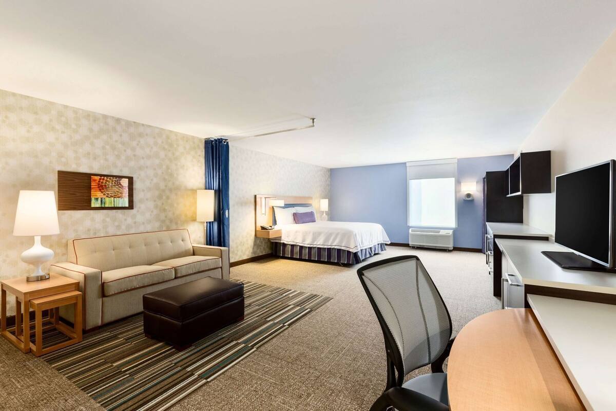 A hotel room with a bed, a sofa, a desk, a TV, and a window.