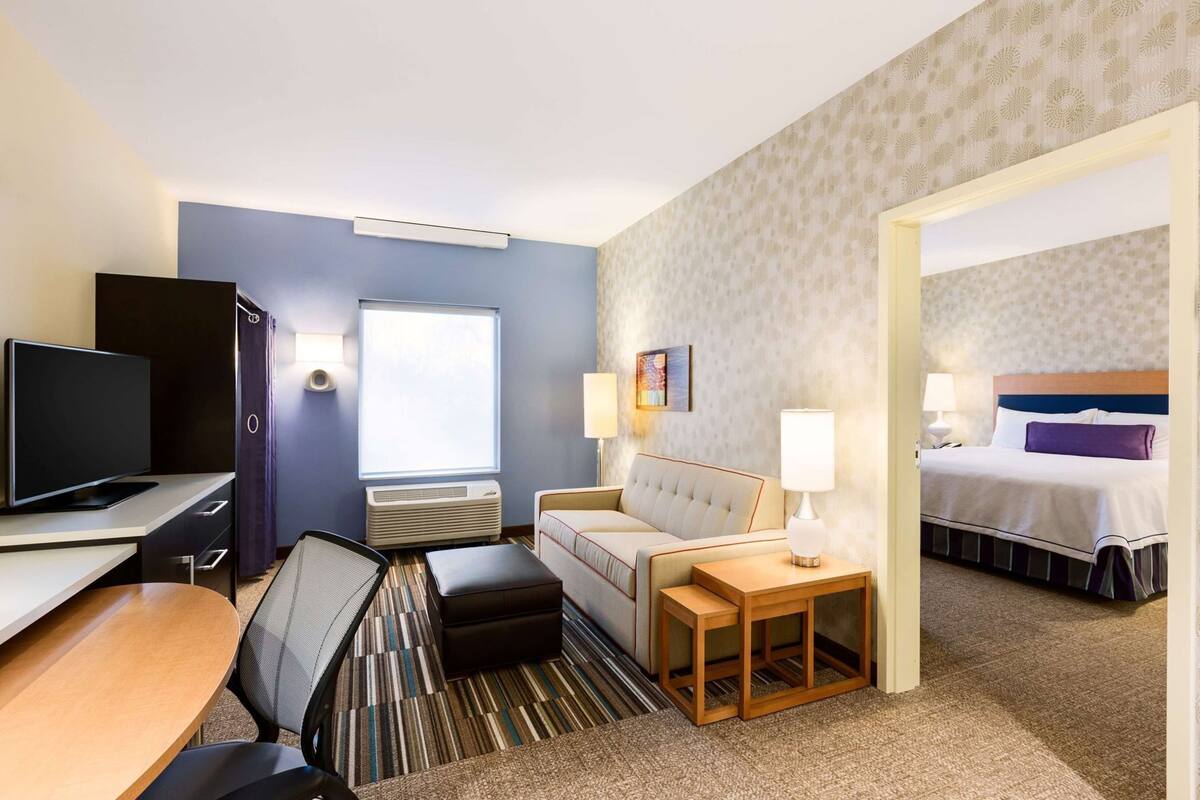 A hotel room with a desk, a sofa, a bed, a television, and a window.