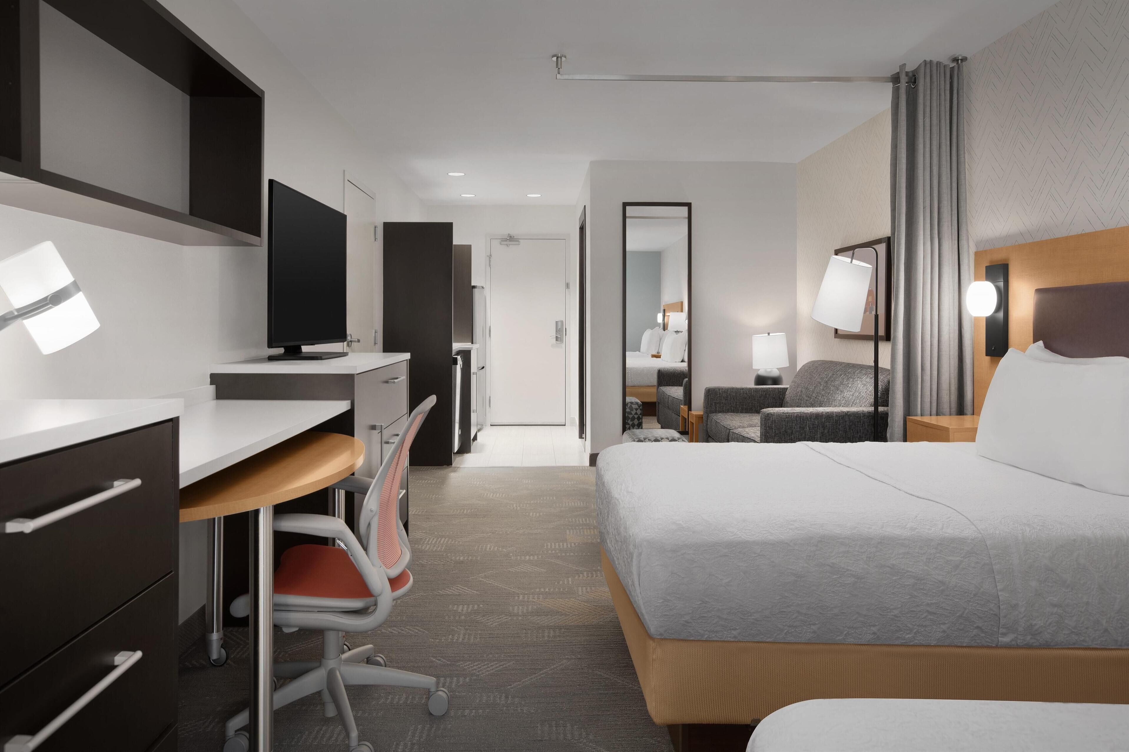 A hotel room with a bed, desk, chair, TV, and a mirror.